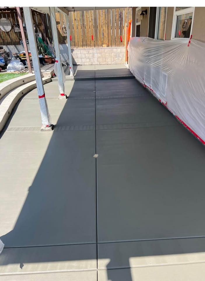 A minimalist outdoor space features three concrete steps leading up to a platform, bordered by a black wooden fence. Tall, green bamboo-like plants create a natural backdrop on one side, complemented by a palm tree on the right—an impeccable design that reflects top-tier concrete services in Glendale AZ.
